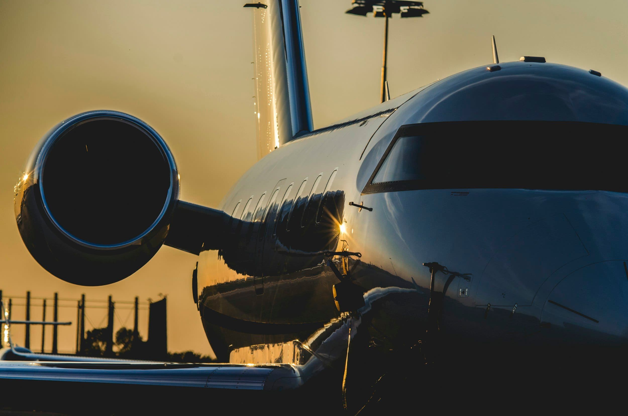 Close-up of a private jet airplane during sunset, showing the engine and sleek, reflective exterior.